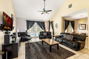 A living room with a black leather sofa, a coffee table, a TV, and a ceiling fan.