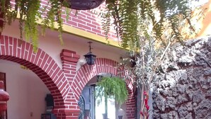 Un espacio interior acogedor con arcos de ladrillo rojo, una mesa de vidrio y diversas plantas en macetas.