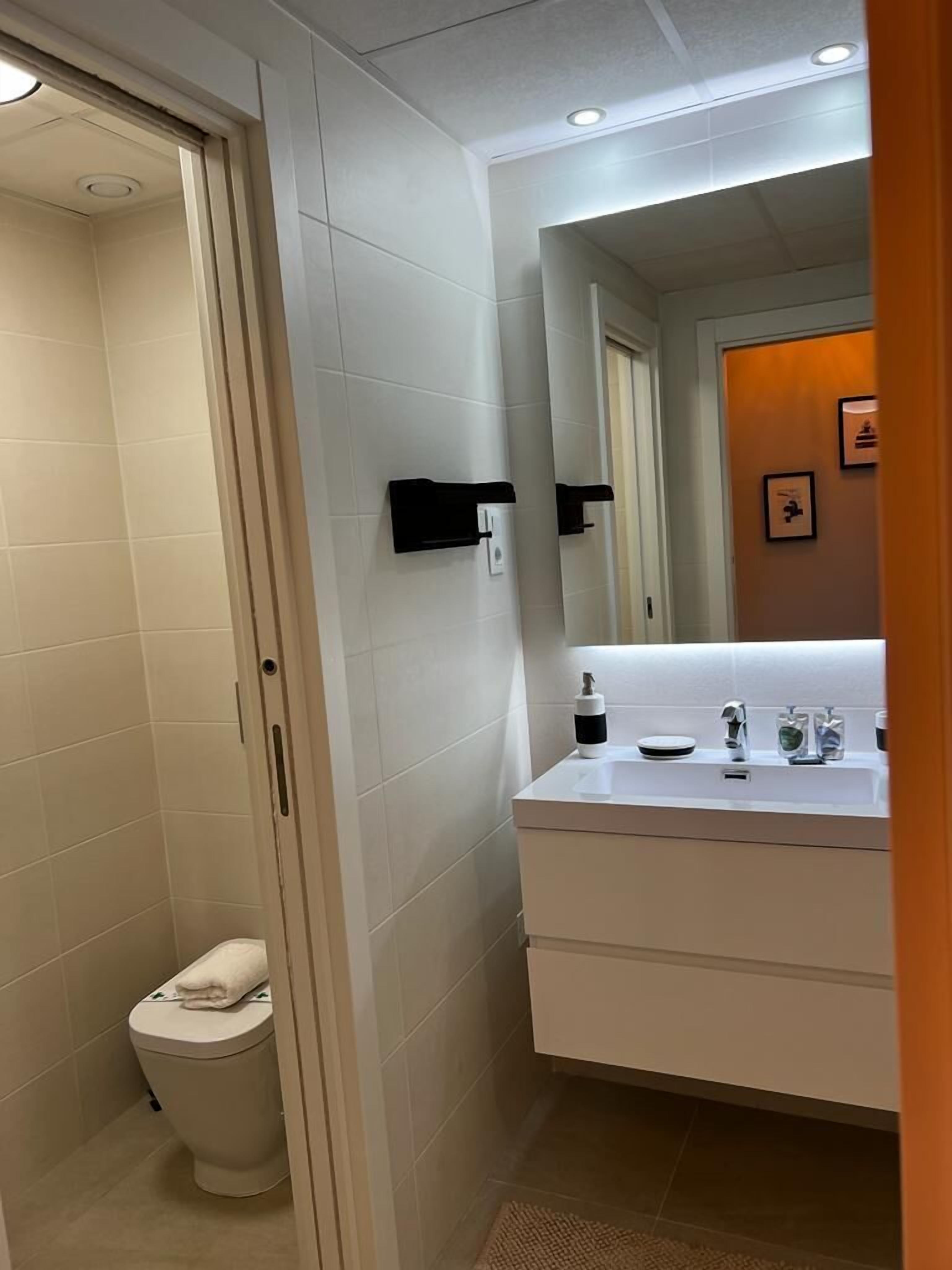 A modern bathroom with a white sink, mirror, and toilet.