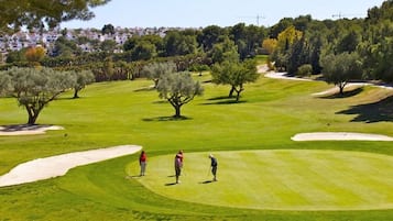 Un campo de golf con búnkeres de arena, árboles y cielo despejado.