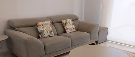 A modern living room with a grey sofa, two floral cushions, a round coffee table, and a patterned rug.