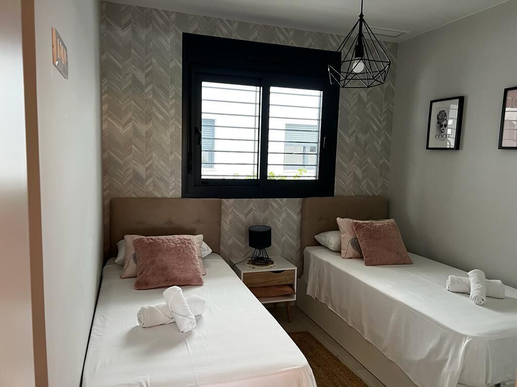 A bedroom with two beds, a window, a nightstand, and a hanging light fixture.