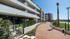 Een modern meerhoogappartementencomplex met een bakstenen pad, groen en een heldere lucht.