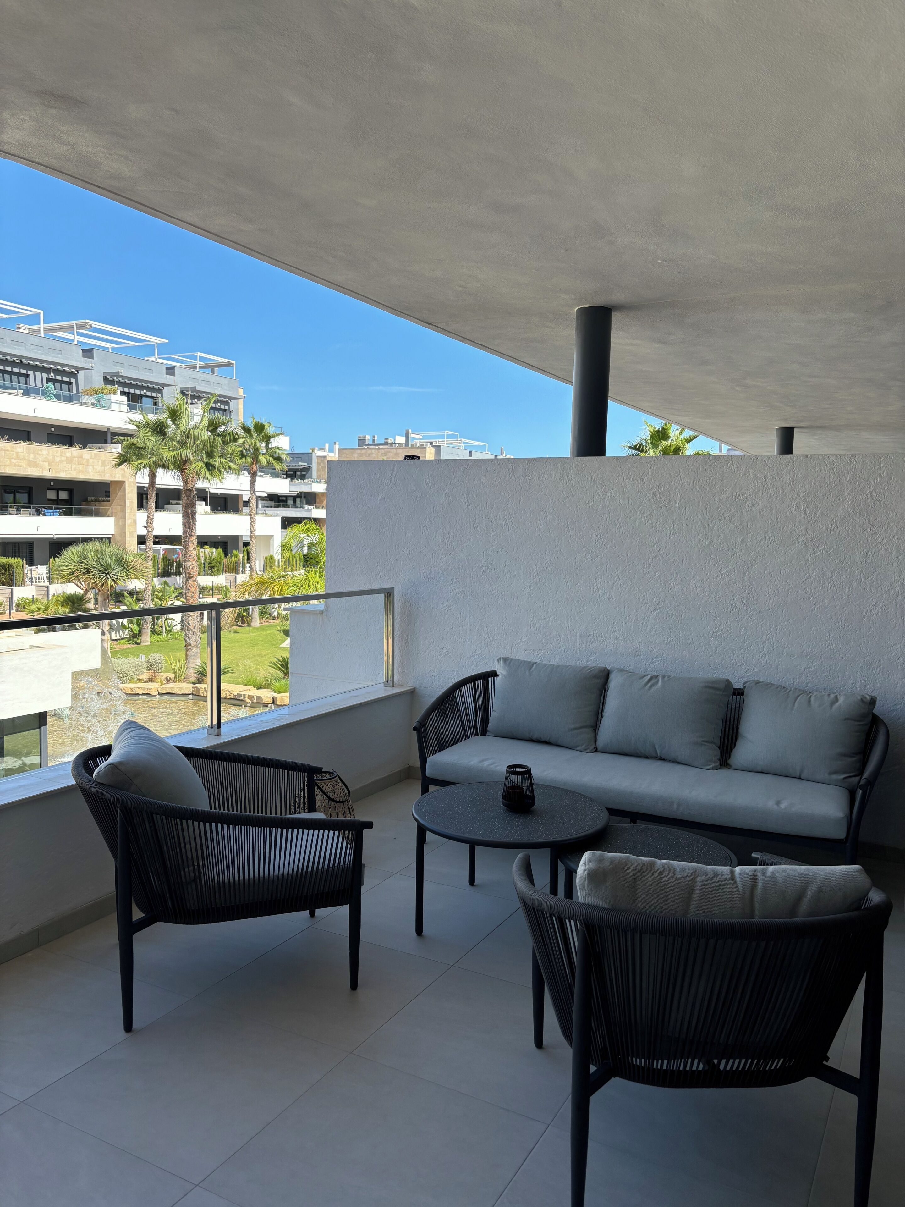 Een balkon met een bank, twee stoelen, een tafeltje en uitzicht op gebouwen en groen.