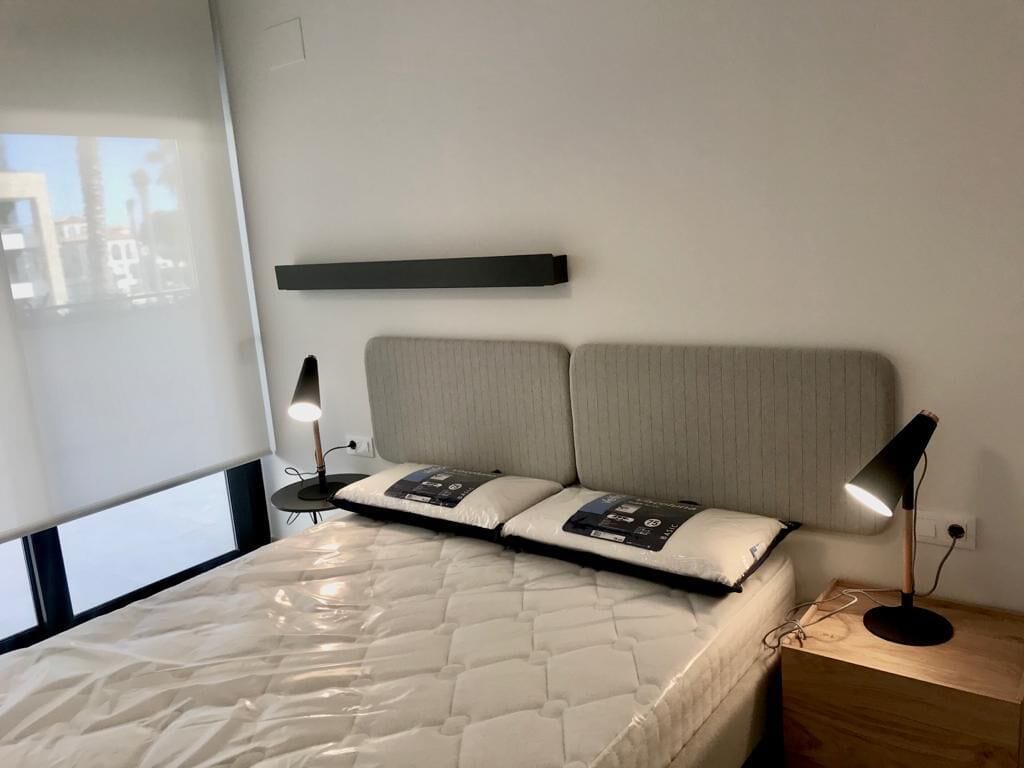 A neatly made bed with a quilted mattress, two bedside lamps, and a headboard with a shelf above.