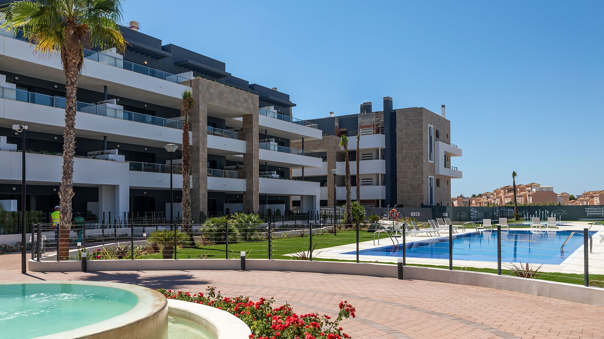A modern multi-story hotel with a swimming pool, outdoor seating, and palm trees.