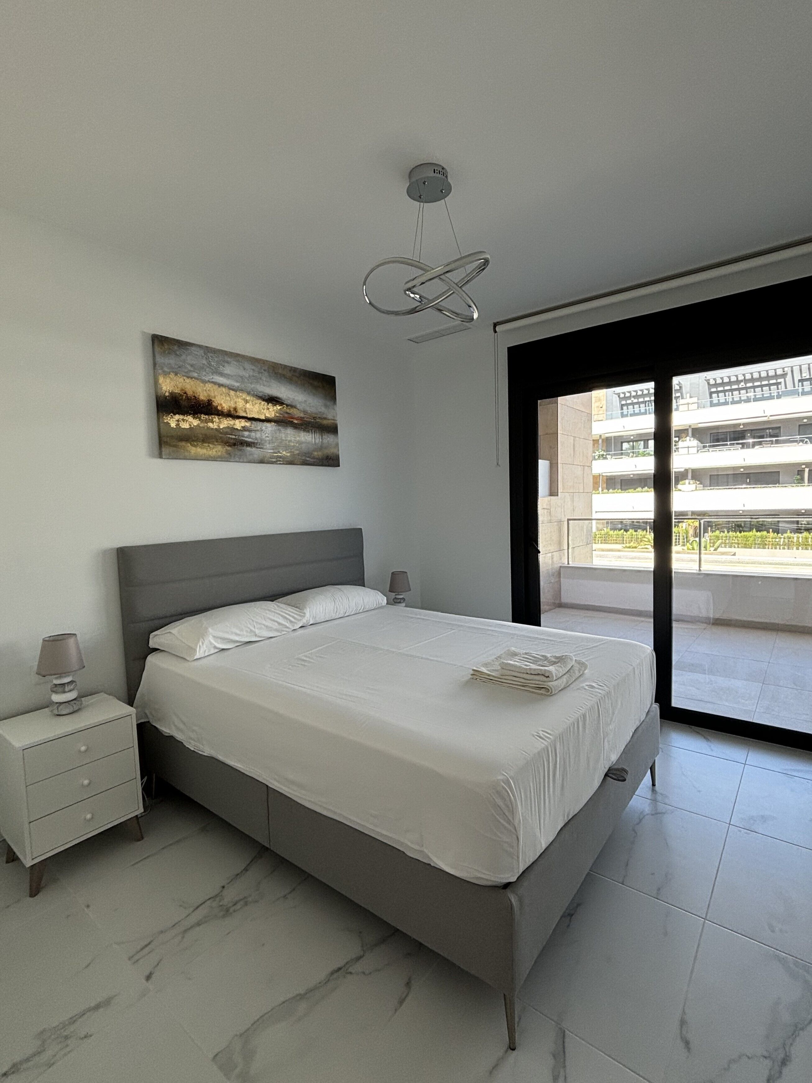 Une chambre à coucher moderne avec un lit, des tables de chevet, un tableau et une vue sur l’extérieur.