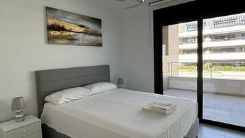 Un dormitorio moderno con cama, mesitas de noche, un cuadro y vistas al exterior.