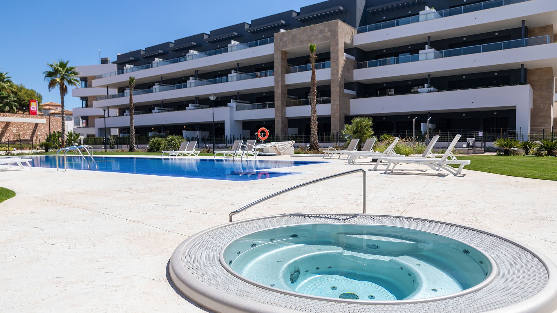 Un hotel con piscina, sillas de descanso y bañera de hidromasaje.