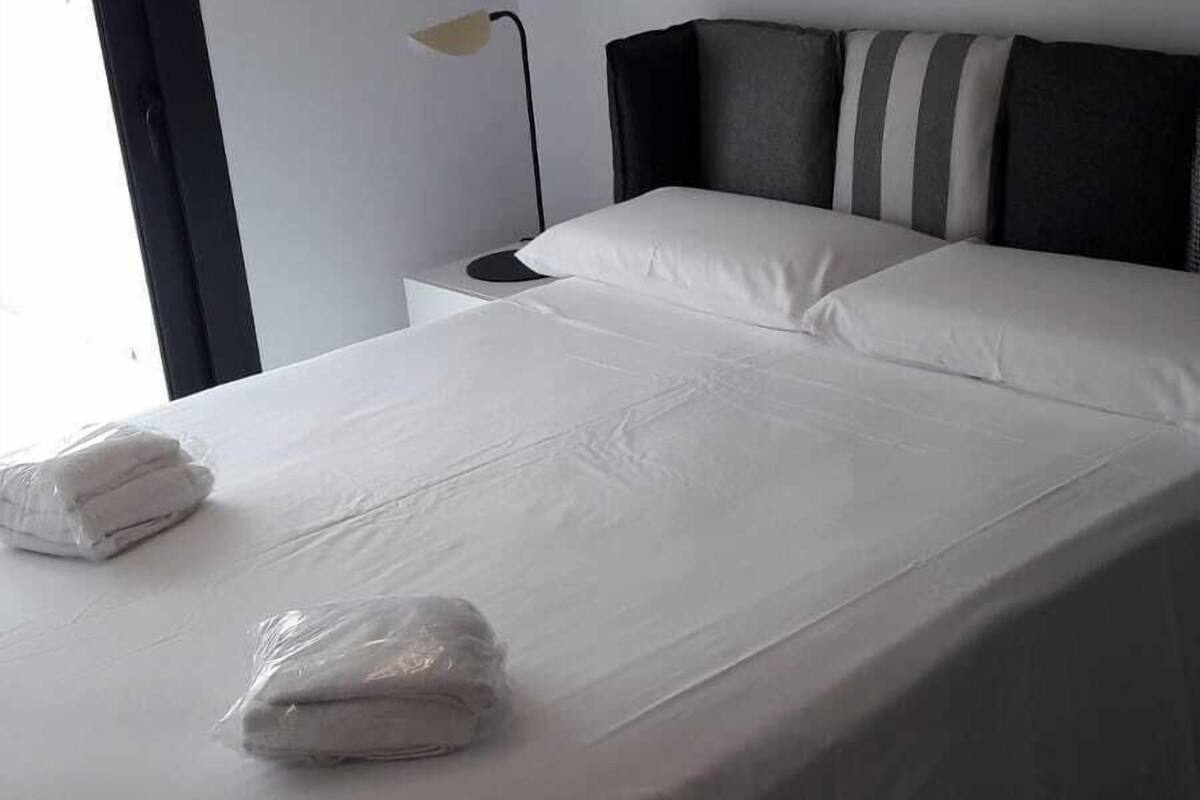 A neatly made bed with white linens and a folded towel, a bedside lamp, and a framed abstract artwork on the wall.