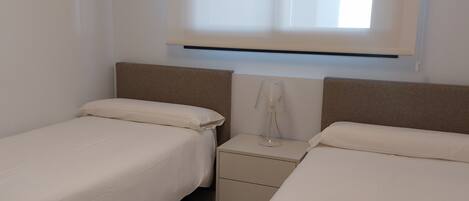 A bedroom with two beds, a nightstand, a lamp, and a window with blinds.