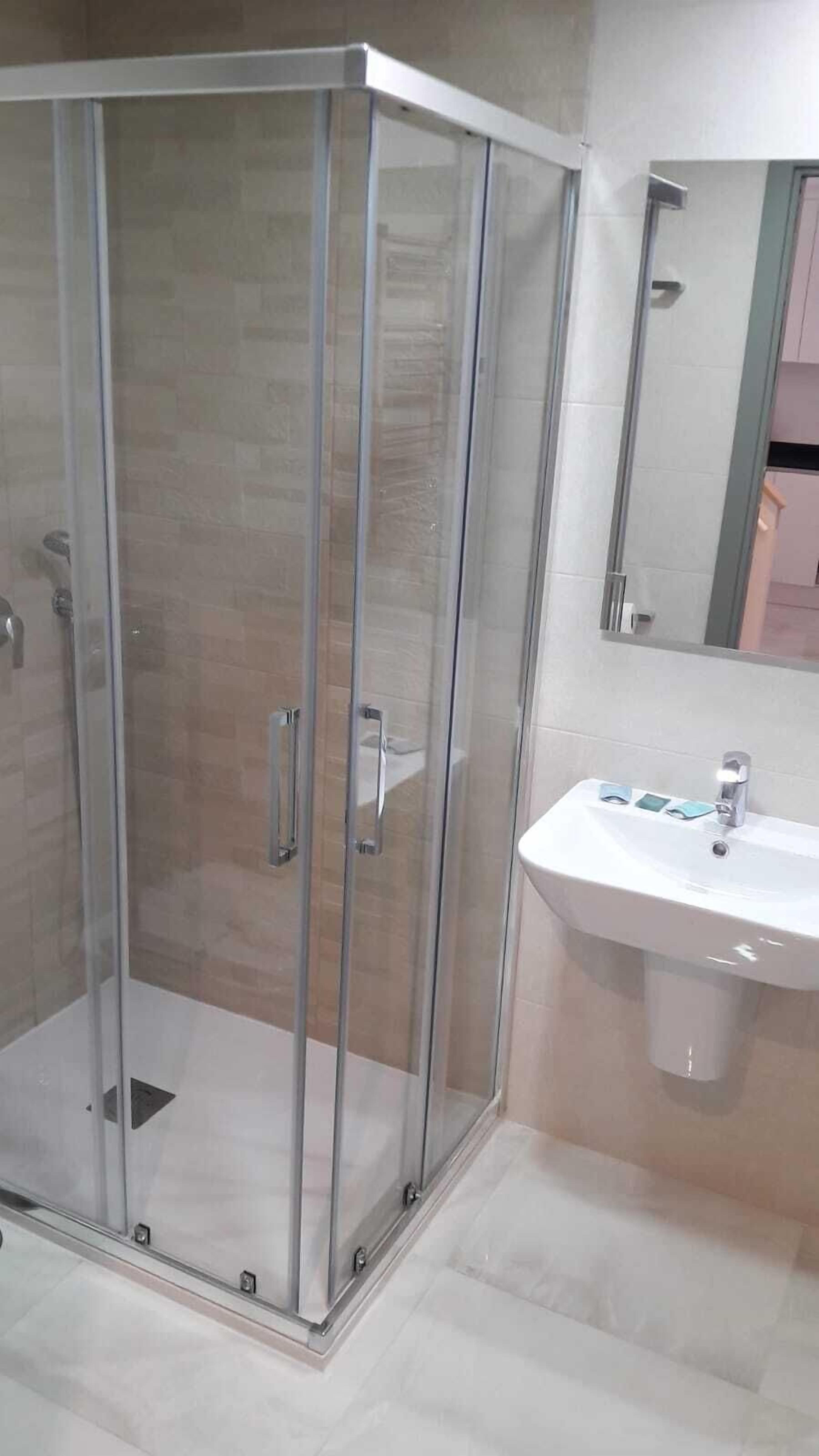 Ein modernes Badezimmer mit einer Duschkabine, einem weißen Waschbecken und einem Spiegel darüber.