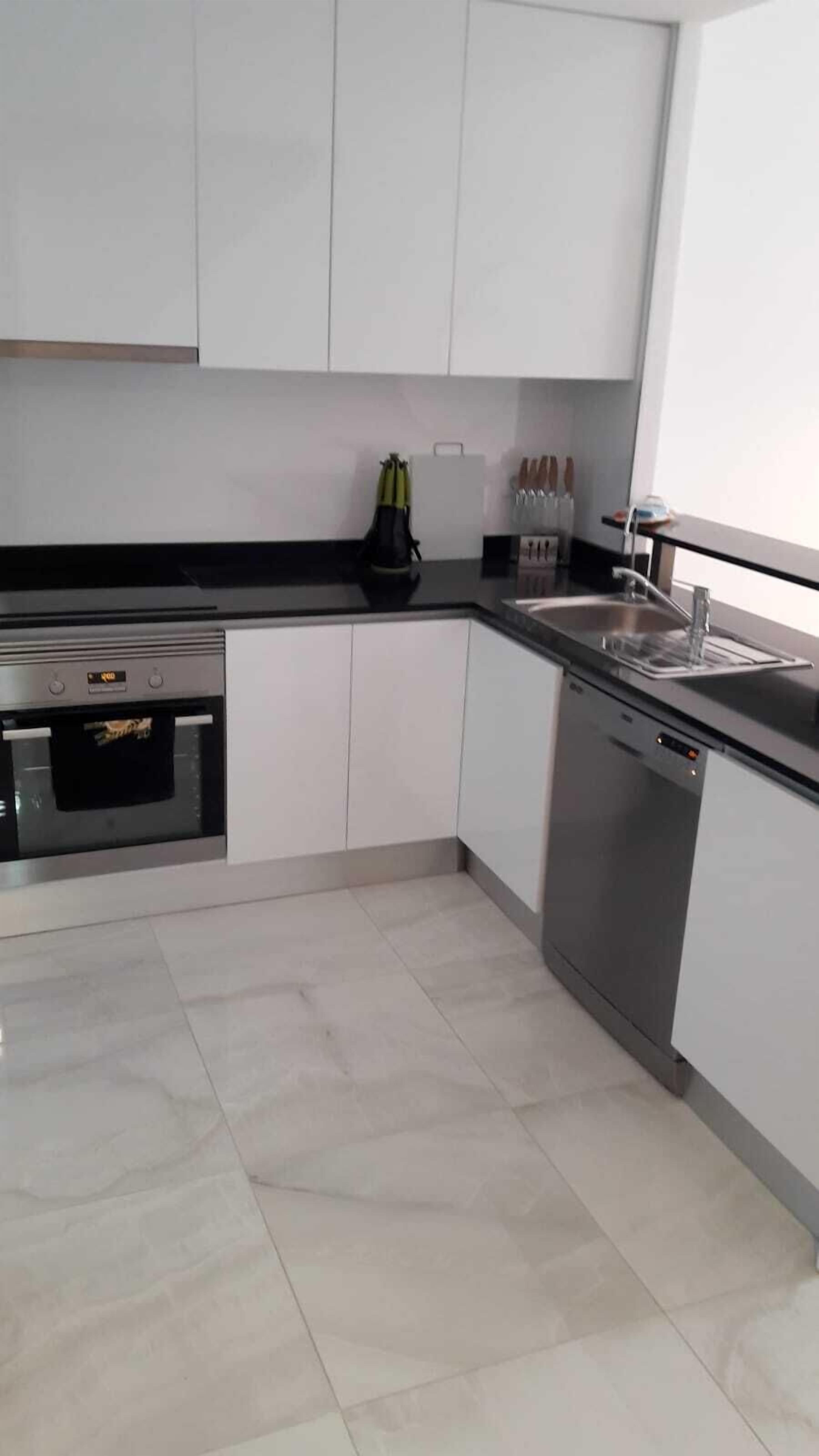 Een moderne keuken met witte kasten, een ingebouwde oven, een vaatwasser en een zwart aanrecht.
