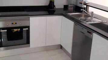 Een moderne keuken met witte kasten, een ingebouwde oven, een vaatwasser en een zwart aanrecht.