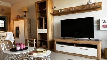 Een woonkamer met een televisie, een houten tv-meubel, rieten stoelen en een ronde salontafel.