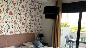 Een hotelkamer met een groot bed, bloemenbehang, een plafondlamp en uitzicht op het buitenbalkon.