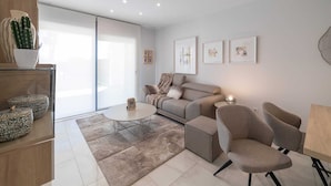 Een moderne woonkamer met een bank, fauteuils, een salontafel en een glazen deur die naar een balkon leidt.