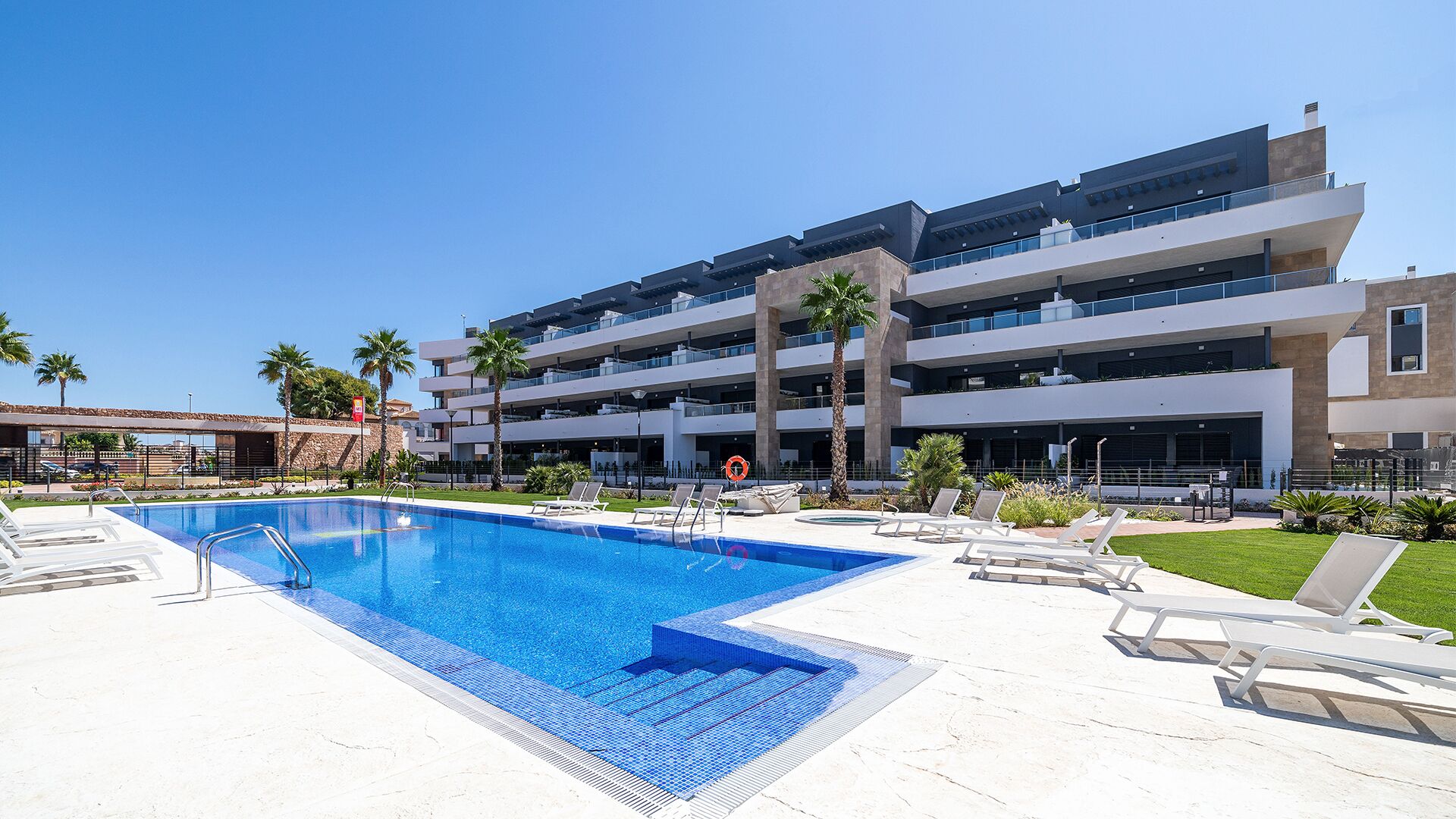 A modern hotel with a swimming pool, multiple balconies, and palm trees.
