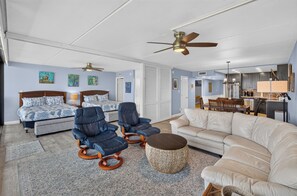 Un salon spacieux comprenant un grand canapé, deux fauteuils, une table basse et un ventilateur de plafond.