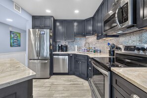 Una cocina moderna con electrodomésticos de acero inoxidable, armarios oscuros y encimera de mármol.