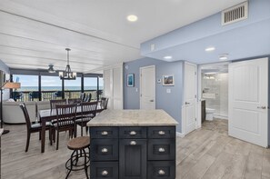 Cocina moderna con una isla grande, comedor con sillas y vista al océano.