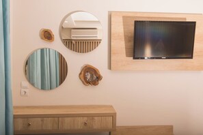 A bathroom with a wooden vanity, a round mirror, and a flat-screen TV mounted on the wall. - Iniohos Zante Hotel & Suites (Zakynthos)