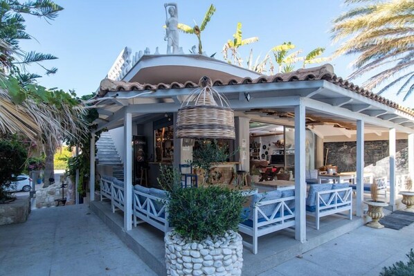 A covered outdoor seating area with stone planters, a wicker basket, and a statue on the roof. - Iniohos Zante Hotel & Suites (Zakynthos)