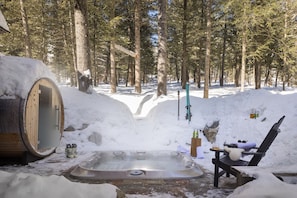 Een hottub in een besneeuwd bos, met een houten vat en een stoel.