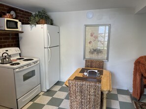 A compact kitchen with a stove, microwave, refrigerator, and a dining table with chairs.
