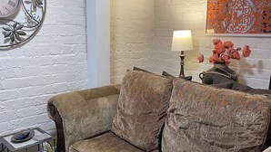 A cozy living room with a brown sofa, a side table with a lamp, and decorative wall art. - Poppies Place @ The Pleasant Street Suites in downtown Prescott (Prescott)