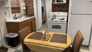 A compact kitchen with a dining table, wicker chairs, a stove, a microwave, and a refrigerator. - Poppies Place @ The Pleasant Street Suites in downtown Prescott (Prescott)