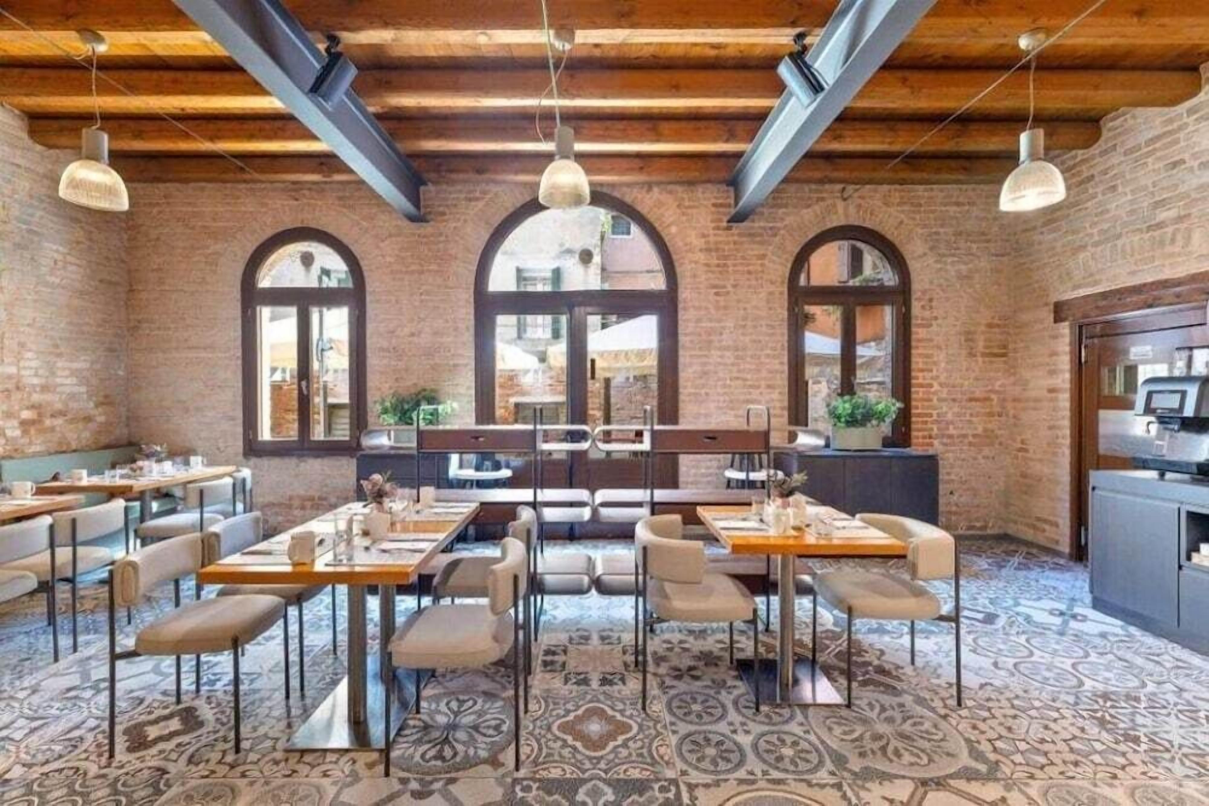 Un restaurante con paredes de ladrillo, ventanas en arco y un suelo con diseño. Mesas y sillas dispuestas para comer.