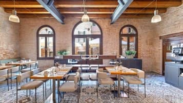 Un restaurante con paredes de ladrillo, ventanas en arco y un suelo con diseño. Mesas y sillas dispuestas para comer.