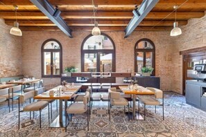 Un restaurant aux murs de briques, aux fenêtres en arc de cercle et au sol orné de motifs. Les tables et les chaises sont disposées pour accueillir les clients.