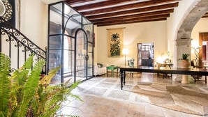 Un intérieur spacieux avec un plafond haut, un escalier doté d’une rampe en fer forgé et un coin repas avec une longue table et des chaises.