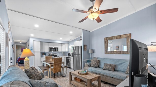 A modern living room with a sofa, coffee table, and a TV. There is a kitchen in the background with cabinets and appliances. - Free Golf Cart, Beach Access/w Parking, + 3 pools! (Surfside Beach)