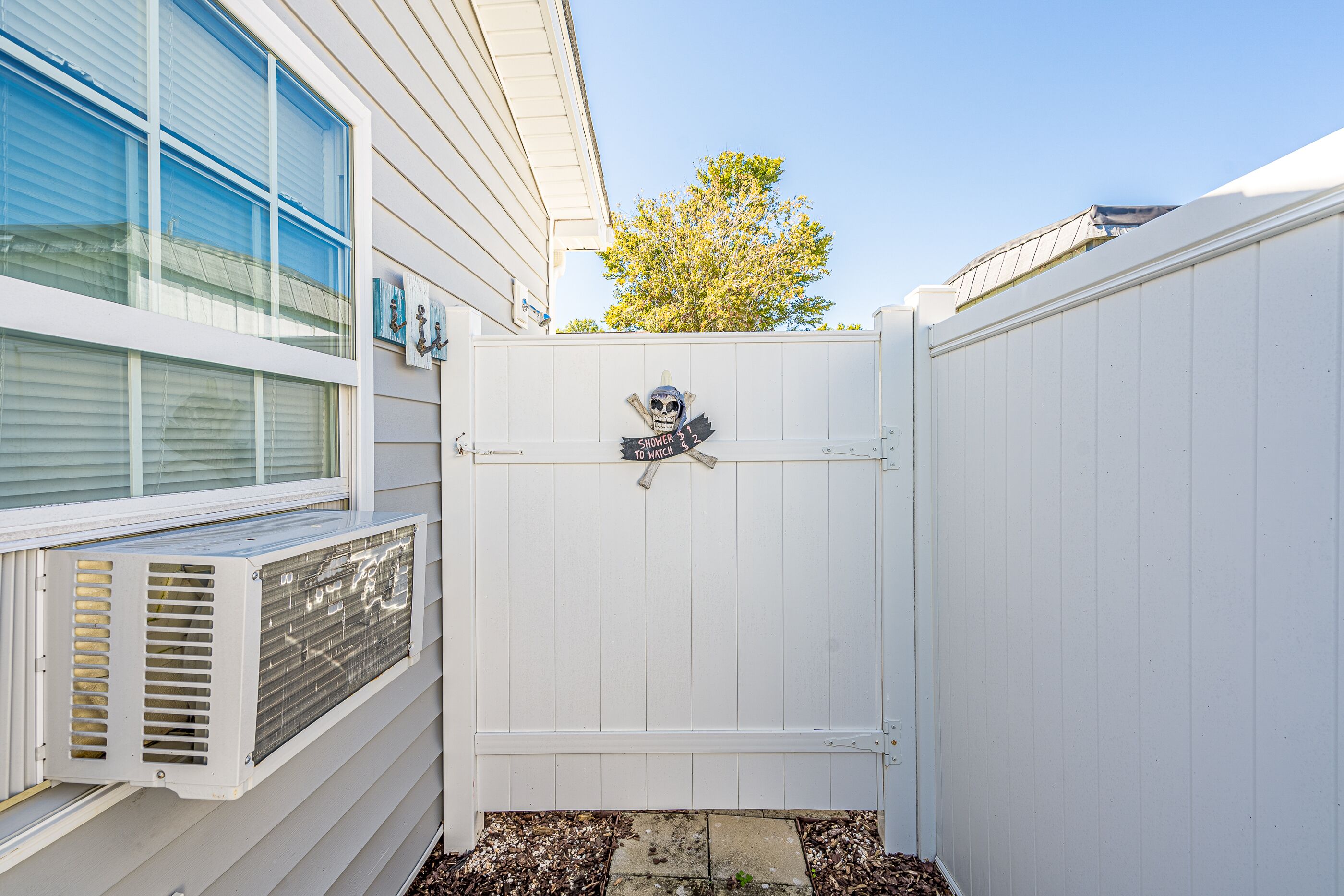 A white fence with a skull and crossbones sign, an air conditioning unit, and a window.