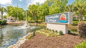 A sign for Oceanside Village with a pond and fountain in the background. - Free Golf Cart, Beach Access/w Parking, + 3 pools! (Surfside Beach)