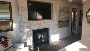 Een moderne woonkamer met een open haard, een grote flatscreen televisie erboven en een gezellige zithoek met een kamerkleed met dessin.