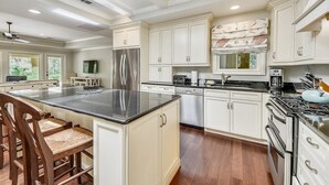 A spacious kitchen with white cabinetry, a large island, stainless steel appliances, and a dining area with wooden chairs. - Beautiful Home w/ Private Pool in Sea Pines (Hilton Head Island)