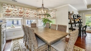 A dining area with a large wooden table, wicker chairs, and a hanging light fixture. - Beautiful Home w/ Private Pool in Sea Pines (Hilton Head Island)