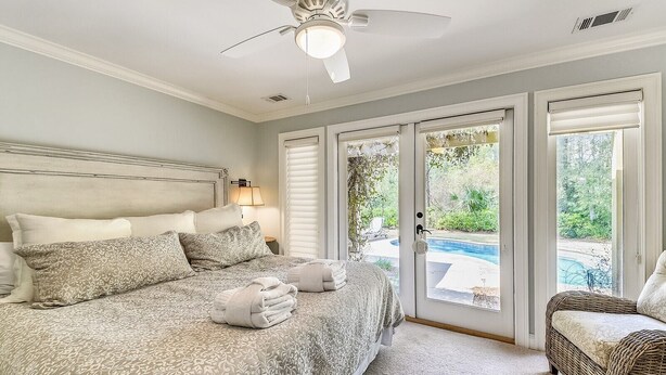 A bedroom with a bed, a ceiling fan, a window with blinds, and a view of a swimming pool. - Beautiful Home w/ Private Pool in Sea Pines (Hilton Head Island)