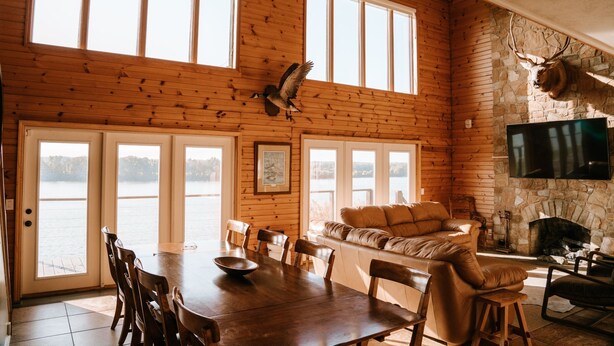 Une cabane dotée d’un coin repas, d’une cheminée et d’une grande fenêtre donnant sur un plan d’eau.