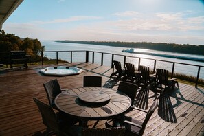 A wooden deck with a round table and chairs, a hot tub, and a view of a river with a boat. - Secluded Ohio River Retreat Retreat with Hot Tub - Sleeps 10 (Elizabethtown)
