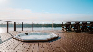 Une terrasse en bois avec un jacuzzi et des fauteuils Adirondack donnant sur une étendue d’eau.