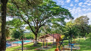 An outdoor exercise area with various fitness equipment, a pool, and a building in the background.