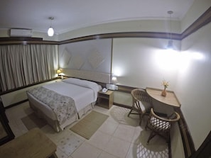 A hotel room with a bed, bedside table, lamp, chair, desk, and a small plant. - Hotel Colonial Iguacu (Foz do Iguaçu)