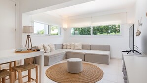 Un ambiente living moderno e minimalista con un divano bianco, un tappeto rotondo in fibra naturale e un'area pranzo con sgabelli di legno.