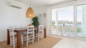 Zona pranzo con tavolo in legno e sedie bianche, lampada pendente in vimini e vista su un porto attraverso ampie vetrate.