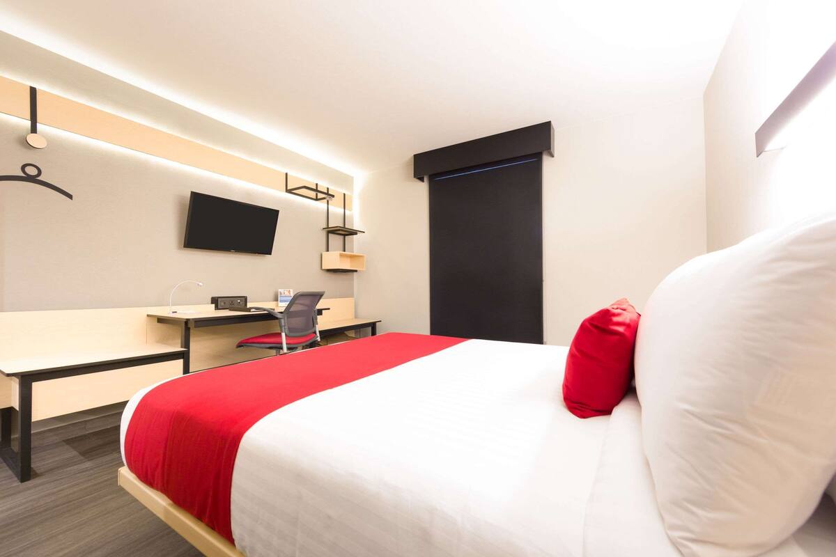 Ett hotellrum med en säng, ett skrivbord, en stol, en tv och ett fönster.